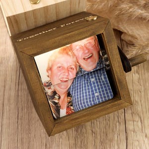 May include: A dark stained wooden photo box with a sliding mechanism, revealing a photograph of a smiling couple. The box is engraved with the words "Together Forever". A small brass clasp secures the lid.