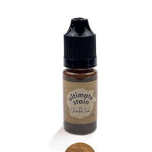 May include: A small brown bottle with a black dropper top. The bottle is labeled "ultimate stain Colorful Soul 9 ml". A small circle shows a sample of the stain, which is a light brown wood color.