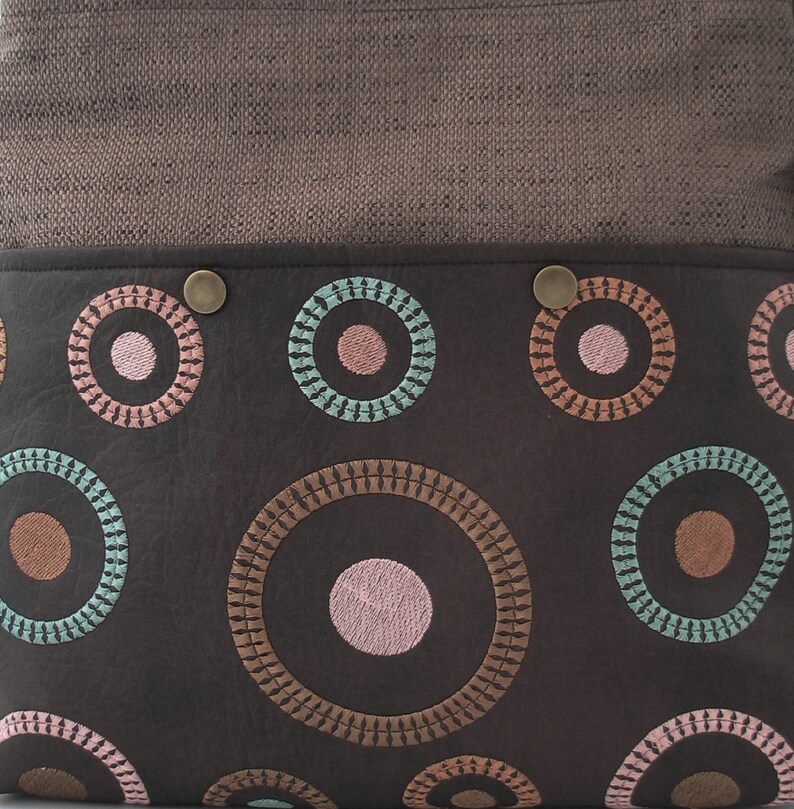 May include: A brown leather bag with a brown fabric flap and a pattern of embroidered circles in shades of pink, teal, and brown.