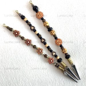May include: Three beaded hair clips with decorative elements. The clips feature a variety of beads in black, brown, and cream colors, along with flower and sun-shaped accents. The clips are finished with silver-colored metal clasps.