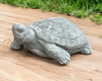 May include: A gray concrete turtle statue with a detailed shell and a realistic appearance. The turtle is lying on its belly with its head turned to the side.