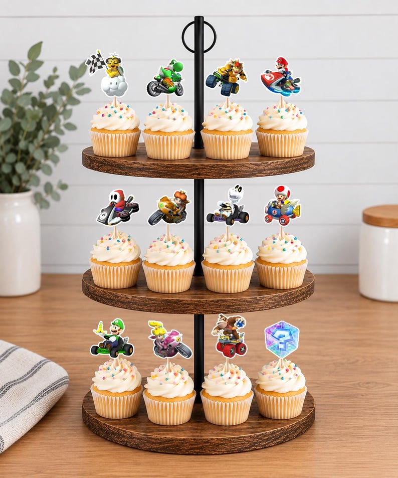 Op de afbeelding: Een houten cupcake-standaard met drie niveaus en twaalf cupcakes, bedekt met witte glazuur en kleurrijke hagelslag. Elke cupcake is voorzien van een decoratieve papieren topper met diverse Mario Kart-personages en items, waaronder racers op voertuigen.
