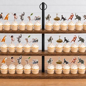 May include: A three-tiered wooden cupcake stand holding rows of cupcakes topped with paper character cutouts. The decorations feature various jungle animals and human figures in colorful illustrations, each attached to a small wooden pick.