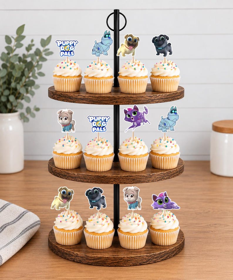 Puede incluir: Un soporte de madera de tres niveles con doce cupcakes cubiertos de glaseado blanco y chispas de colores. Cada cupcake tiene un adorno de papel con personajes y el texto Puppy Dog Pals de la serie de animaci&oacute;n.