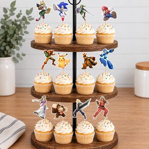 Pu&ograve; includere: Un'alzata per cupcake in legno a tre livelli con dodici cupcake, ognuno guarnito con un ciuffo di glassa bianca, zuccherini colorati e una sagoma di carta di un personaggio dei videogiochi come Mario, Sonic o Pikachu.