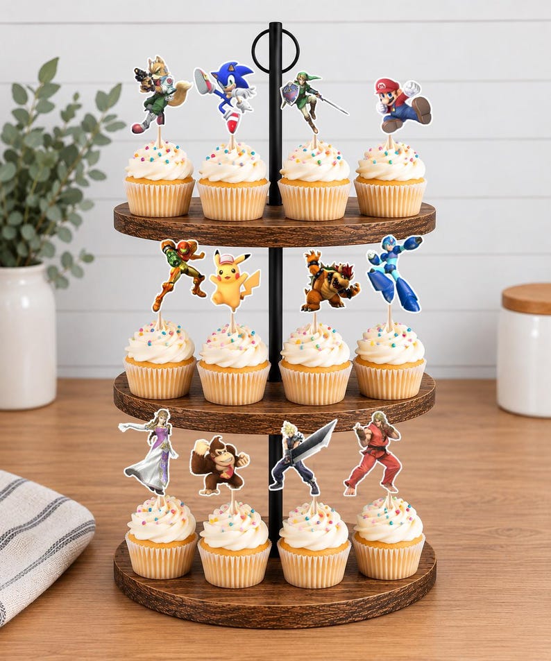 Pu&ograve; includere: Un'alzata per cupcake in legno a tre livelli con dodici cupcake, ognuno guarnito con un ciuffo di glassa bianca, zuccherini colorati e una sagoma di carta di un personaggio dei videogiochi come Mario, Sonic o Pikachu.