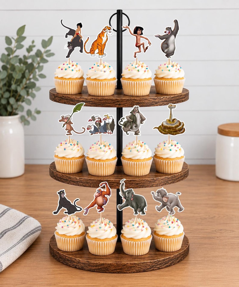May include: A three-tiered wooden cupcake stand holding twelve cupcakes, each topped with a white frosting swirl and colorful sprinkles. Each cupcake features a decorative paper topper depicting various animated characters from The Jungle Book.