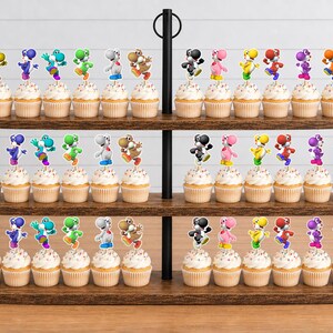 May include: A three-tiered wooden cupcake stand holding numerous cupcakes topped with colourful Yoshi character paper toppers. The toppers feature various Yoshi figures in yellow, blue, teal, green, white, brown, black, pink, and orange colours.