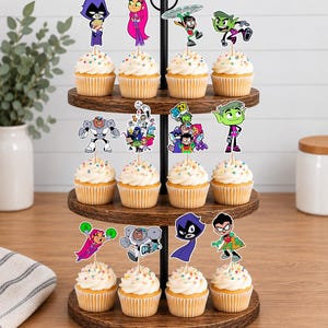 May include: A three-tiered wooden cupcake stand holding twelve cupcakes topped with white frosting and colourful sprinkles. Each cupcake features a paper topper depicting various Teen Titans Go characters, including Raven, Starfire, Robin, Cyborg, and Beast Boy.