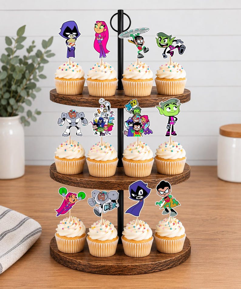 May include: A three-tiered wooden cupcake stand holding twelve cupcakes topped with white frosting and colourful sprinkles. Each cupcake features a paper topper depicting various Teen Titans Go characters, including Raven, Starfire, Robin, Cyborg, and Beast Boy.