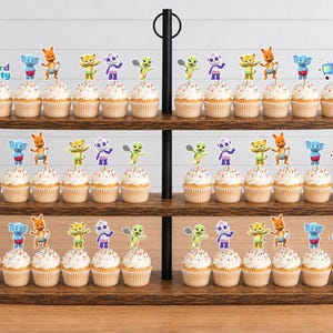 Puede incluir: Un soporte de madera de tres niveles para cupcakes que muestra numerosos pastelitos decorados con recortes de papel coloridos de los personajes de Word Party, incluyendo a Lulu, Bailey, Franny, Kip y Tilly. Cada cupcake tiene glaseado blanco.