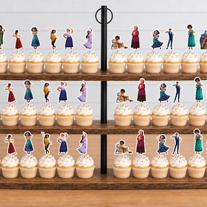 Pode incluir: Um suporte de madeira para cupcakes de tr&ecirc;s n&iacute;veis com v&aacute;rios cupcakes decorados com recortes de papel de v&aacute;rios personagens do filme Encanto. Os personagens incluem Mirabel, Isabela, Luisa, Bruno e a casa Casita.