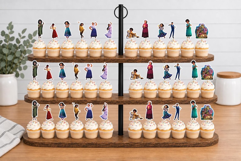 Pode incluir: Um suporte de madeira para cupcakes de tr&ecirc;s n&iacute;veis com v&aacute;rios cupcakes decorados com recortes de papel de v&aacute;rios personagens do filme Encanto. Os personagens incluem Mirabel, Isabela, Luisa, Bruno e a casa Casita.