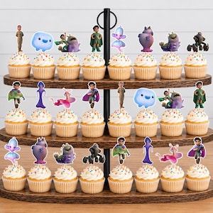 May include: A three-tiered wooden cupcake stand holding twenty-four cupcakes, each topped with a colourful character cutout. The toppers feature various animated figures, including small humanoids, blue blobs, and purple creatures, arranged in rows.