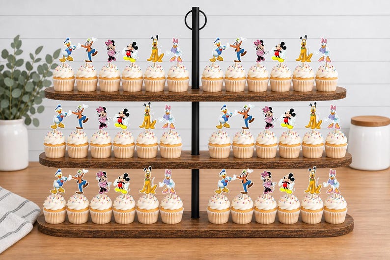 May include: A three-tiered wooden cupcake stand holding numerous cupcakes topped with colorful paper cutouts of various cartoon characters, including Mickey Mouse, Minnie Mouse, Donald Duck, Goofy, Pluto, and Daisy Duck, arranged in rows.