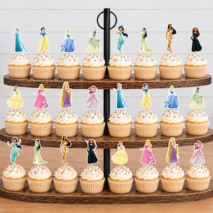May include: A three-tiered wooden cupcake stand holding twenty-three cupcakes, each topped with a unique paper cutout of a different female character in a colorful gown. The cupcakes feature white frosting with multicolored sprinkles in paper liners.
