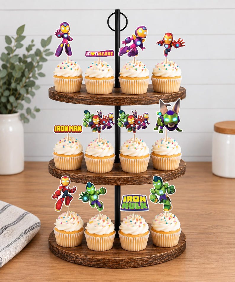 May include: A three-tiered wooden cupcake stand holding twelve cupcakes topped with colorful sprinkles and various superhero-themed paper toppers, including characters like Iron Man, Ironheart, and Iron Hulk, with text labels reading Ironheart, Ironman, and Iron Hulk.