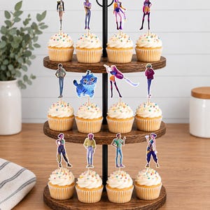 Op de afbeelding: Een houten cupcake-standaard met drie niveaus en twaalf cupcakes, bedekt met witte glazuur en kleurrijke hagelslag. Elke cupcake is voorzien van een decoratieve papieren topper met diverse geanimeerde figuren, waaronder een blauw katachtig wezen.