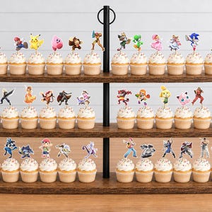 May include: A three-tiered wooden cupcake stand holding numerous cupcakes, each topped with a unique paper cutout of a video game character. The characters include various figures from popular gaming franchises, arranged across the three shelves.