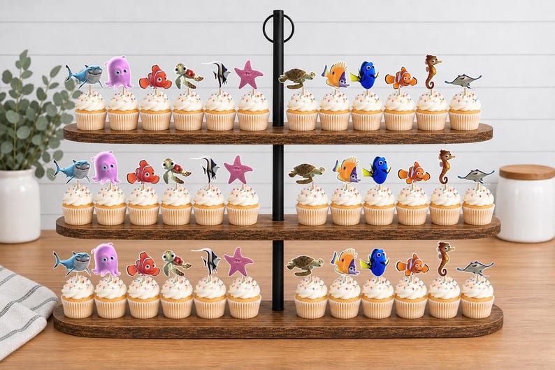 May include: A three-tiered wooden cupcake stand holding rows of cupcakes topped with various sea creature character cutouts, including a shark, octopus, clownfish, sea turtle, angelfish, starfish, blue tang, seahorse, and stingray.