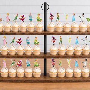 May include: A three-tiered wooden cupcake stand holding numerous cupcakes topped with colorful paper character cutouts. The decorations feature various figures including a boy in green, a fairy, a pirate, and a crocodile, arranged in rows.