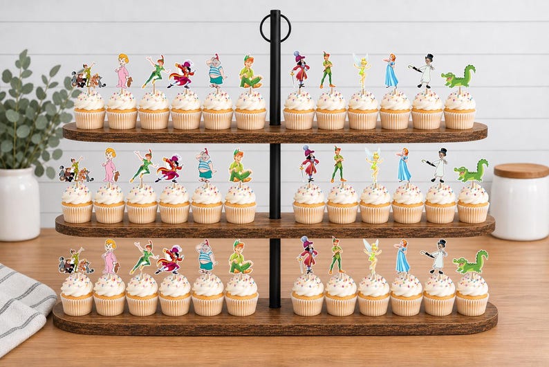 May include: A three-tiered wooden cupcake stand holding numerous cupcakes topped with colorful paper character cutouts. The decorations feature various figures including a boy in green, a fairy, a pirate, and a crocodile, arranged in rows.
