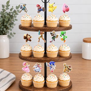 May include: A three-tiered wooden cupcake stand holding twelve cupcakes, each topped with a colorful paper cutout of a video game character. The characters include Mario, Pikachu, Kirby, Link, Donkey Kong, Samus, Fox, Yoshi, Peach, Zelda, Sonic, and Bowser.