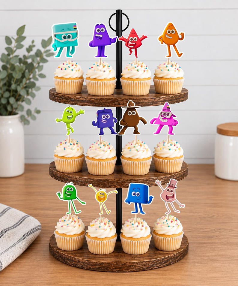 May include: A three-tiered wooden cupcake stand holding twelve cupcakes topped with white frosting and colorful sprinkles. Each cupcake features a unique, colorful cartoon character topper in various shapes including squares, triangles, and circles.
