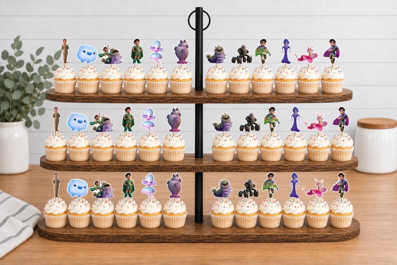 May include: A three-tiered wooden cupcake stand holding rows of cupcakes topped with various character-themed paper toppers. The toppers feature colourful illustrations of diverse figures, creatures, and abstract shapes, each attached to a small pick.