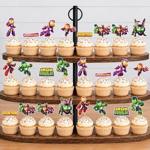 May include: A three-tiered wooden cupcake stand holding twenty-four cupcakes topped with colorful paper toppers featuring various superhero characters and text including Iron Man, Ironheart, and Iron Hulk in vibrant red, green, and purple hues.