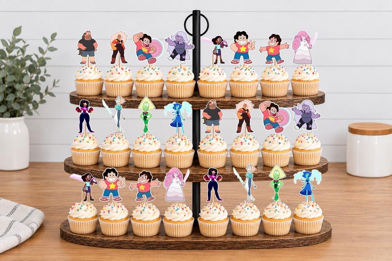 Puede incluir: Un soporte de madera para cupcakes de tres niveles con veinticuatro cupcakes, cada uno decorado con un recorte de papel colorido de un personaje de la serie animada Steven Universe. Los cupcakes tienen glaseado blanco con chispas de colores.