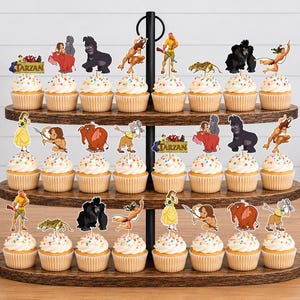 May include: A three-tiered wooden cupcake stand holding numerous cupcakes topped with colorful sprinkles and paper cutouts of characters from the movie Tarzan, including Tarzan, Jane, and various jungle animals, with the word Tarzan printed on signs.