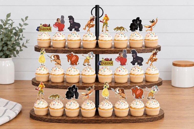 May include: A three-tiered wooden cupcake stand holding numerous cupcakes topped with colorful sprinkles and paper cutouts of characters from the movie Tarzan, including Tarzan, Jane, and various jungle animals, with the word Tarzan printed on signs.