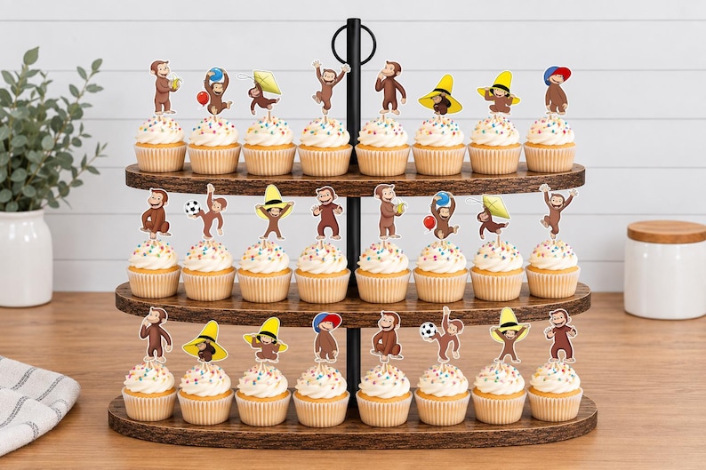 May include: A three-tiered wooden cupcake stand holding twenty-four cupcakes, each topped with a paper cutout of Curious George in various poses, including wearing hats, holding balloons, playing with a soccer ball, or flying a kite.