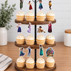 Pode incluir: Um suporte de madeira para cupcakes de tr&ecirc;s n&iacute;veis com doze cupcakes cobertos com cobertura branca e granulado colorido. Cada cupcake possui um topo de papel decorativo retratando v&aacute;rios personagens e uma casa do filme Encanto.