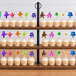 May include: A three-tiered wooden cupcake stand holding rows of cupcakes topped with colorful, cartoon-style character toppers. The toppers feature various shapes and vibrant colors, including blue, purple, red, orange, green, brown, and pink figures.