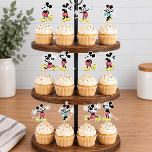 K&ouml;nnte beinhalten: Ein dreist&ouml;ckiger Cupcake-St&auml;nder aus Holz mit zw&ouml;lf Cupcakes, die jeweils mit einem dekorativen Papieraufsteller von Mickey Mouse in verschiedenen Posen verziert sind. Die Cupcakes haben eine wei&szlig;e Glasur mit bunten Streuseln.