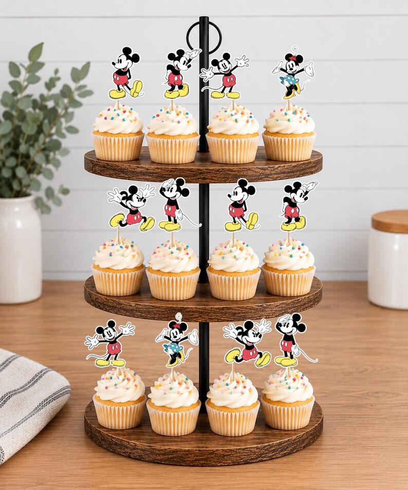 K&ouml;nnte beinhalten: Ein dreist&ouml;ckiger Cupcake-St&auml;nder aus Holz mit zw&ouml;lf Cupcakes, die jeweils mit einem dekorativen Papieraufsteller von Mickey Mouse in verschiedenen Posen verziert sind. Die Cupcakes haben eine wei&szlig;e Glasur mit bunten Streuseln.