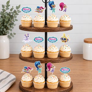 May include: A three-tiered wooden cupcake stand holding twelve cupcakes topped with white frosting, colorful sprinkles, and Shimmer and Shine character paper toppers. The toppers feature various characters, animals, and the Shimmer and Shine logo.