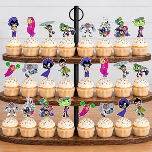 May include: A three-tiered wooden cupcake stand holding twenty-four cupcakes, each topped with a colourful paper cutout of Teen Titans characters including Raven, Starfire, Robin, Beast Boy, and Cyborg, featuring multi-coloured sprinkles on white frosting.