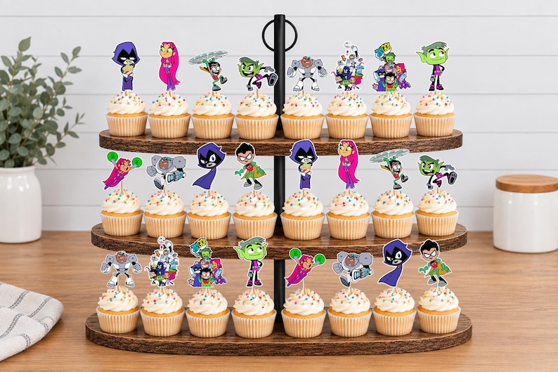 May include: A three-tiered wooden cupcake stand holding twenty-four cupcakes, each topped with a colourful paper cutout of Teen Titans characters including Raven, Starfire, Robin, Beast Boy, and Cyborg, featuring multi-coloured sprinkles on white frosting.