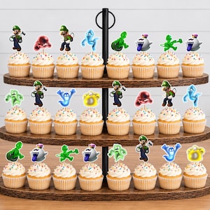 Puede incluir: Un soporte de madera para cupcakes de tres niveles con veinticuatro cupcakes, cada uno decorado con un recorte de papel que muestra personajes y fantasmas de la serie de videojuegos Luigi's Mansion, incluyendo a Luigi y varias figuras espectrales.