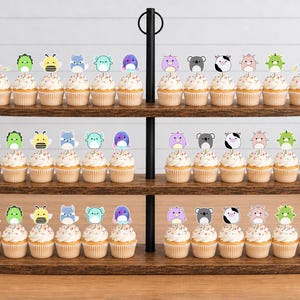 May include: A three-tiered wooden cupcake stand holding rows of cupcakes topped with colorful animal-shaped paper toppers. The toppers feature various creatures including bees, koalas, cows, and dragons, each attached to a small wooden pick.