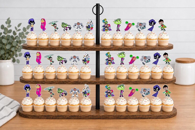 May include: A three-tiered wooden cupcake stand holding numerous cupcakes topped with colourful paper cutouts of Teen Titans characters including Raven, Starfire, Robin, Beast Boy, and Cyborg, each featuring vibrant illustrations on wooden picks.
