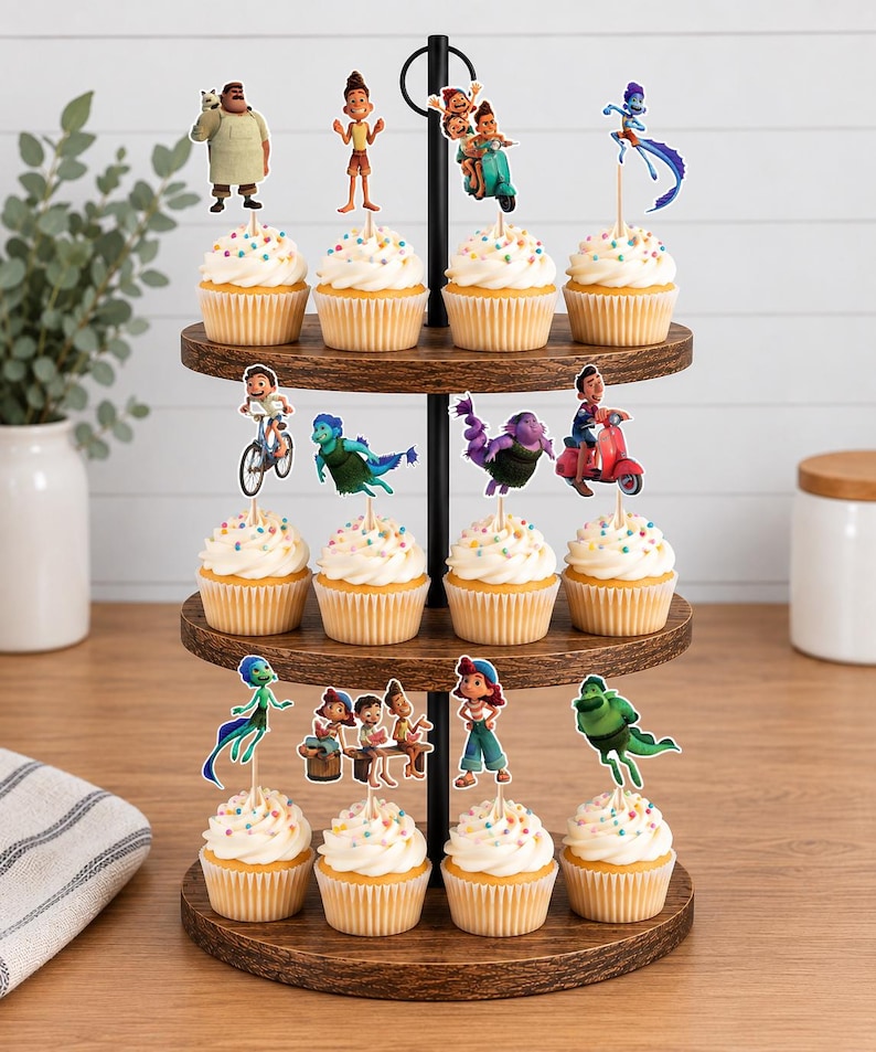Puede incluir: Un soporte de madera de tres niveles con doce cupcakes cubiertos de glaseado blanco y chispas de colores. Cada cupcake tiene un adorno de papel &uacute;nico que representa a varios personajes de la pel&iacute;cula Luca.