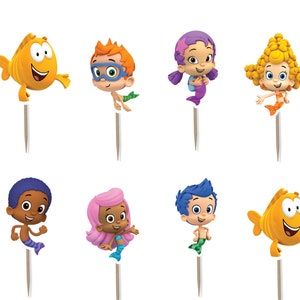 May include: A collection of colorful cupcake toppers featuring characters from the animated series, Bubble Guppies. The toppers include various characters and round toppers with the show's logo on a blue background. Each topper is attached to a wooden stick.