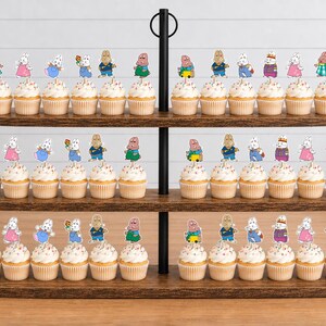 May include: A three-tiered wooden cupcake stand holding numerous cupcakes topped with decorative paper cutouts of cartoon rabbit characters in various colorful outfits, including blue, pink, and green clothing, arranged in rows on each shelf.