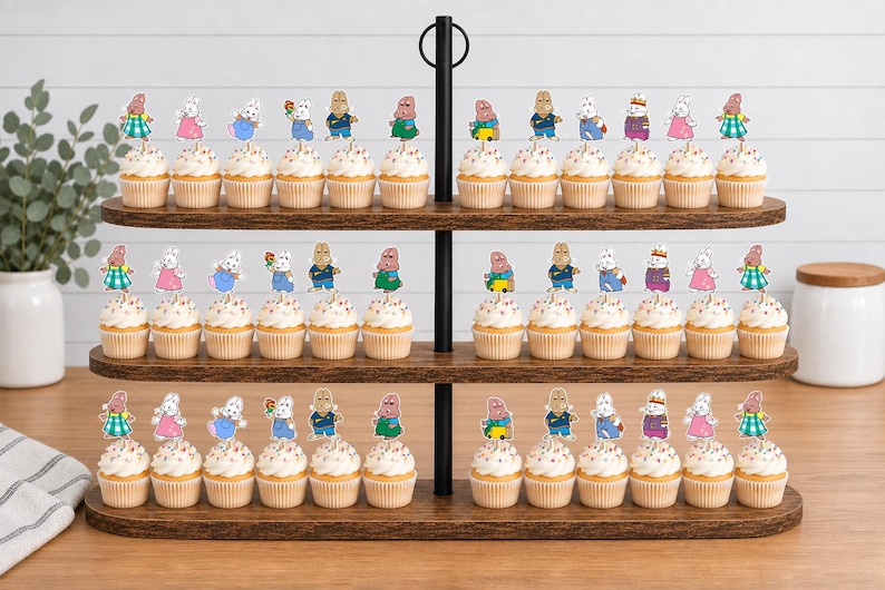 May include: A three-tiered wooden cupcake stand holding numerous cupcakes topped with decorative paper cutouts of cartoon rabbit characters in various colorful outfits, including blue, pink, and green clothing, arranged in rows on each shelf.