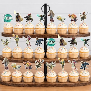 May include: A three-tiered wooden cupcake stand holding twenty-four cupcakes, each topped with a decorative paper cutout featuring characters and the Legend of Zelda logo. The cupcakes have white frosting with colourful sprinkles on a brown wooden stand.