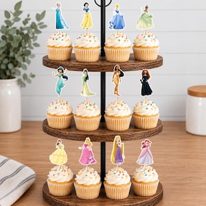 May include: A three-tiered wooden cupcake stand holding twelve cupcakes, each topped with a decorative paper cutout of a different animated princess character. The stand features a central black metal rod and circular wooden shelves with a dark wood grain finish.